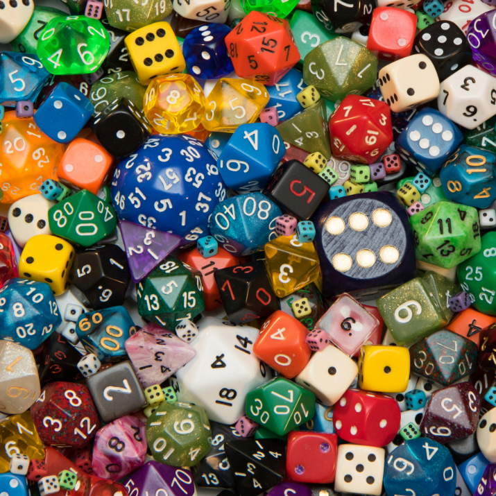 A dense, colorful assortment of polyhedral gaming dice in various shapes, sizes, and colors, including red, blue, green, purple, orange, yellow, and white, filling the entire frame.